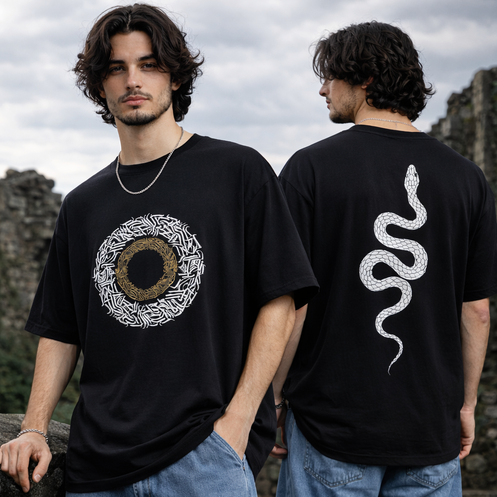 Person wearing a black t-shirt with a circular design on the front and a snake on the back, standing against a stone wall.